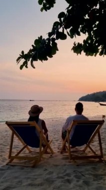 Çiftler tropikal plajda gün batımını izliyorlar, Asyalı kadınlar ve Koh Lipe Tayland sahilinde bir sandalyede beyaz erkekler..