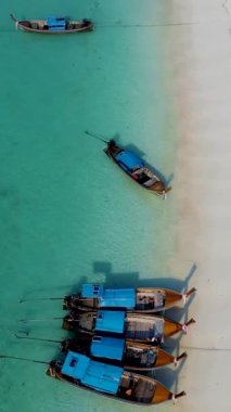 Tayland 'ın Koh Lipe şehrinde güneşli bir günde, turkuaz renkli okyanusta uzun kuyruklu teknelerin Koh Lipe Adası manzarası. Kumsaldaki hava aracı görüntüsü.