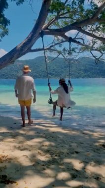 Ko Ra Wi Adası Tarutao Ulusal Parkı, Satun Eyaleti, Tayland sahilinde ip salıncaklı bir çift kadın ve erkek.