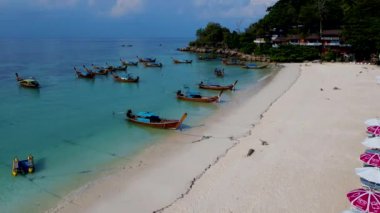 Tayland 'daki Koh Lipe Adası' nda güneşli bir günde turkuaz renkli okyanusta uzun kuyruklu teknelerin hava manzarası. Kumsaldaki hava aracı görüntüsü.