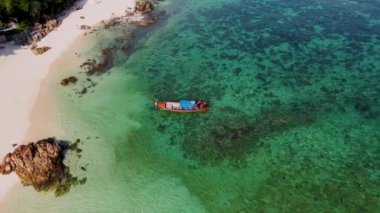 Tayland 'daki Koh Lipe Adası' nda güneşli bir günde turkuaz renkli okyanusta uzun kuyruklu teknelerin hava manzarası. Beyaz kum ve mavi okyanusla kumsalda drone hava manzarası