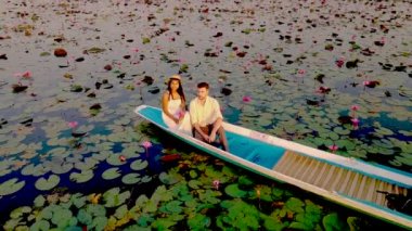 Gündoğumu Kızıl Nilüfer Denizi, Nong Harn Gölü, Udon Thani, Tayland. Tayland 'daki Red Lotus Gölü' nde gün doğumunda ahşap bir teknede bir çift kadın ve erkek İHA 'dan görülmüş.