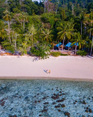 Güney Tayland 'daki Koh Kradan Adası plajında bir çift adam ve kadın. Koh Kradan sahilinde palmiye ağaçları ve mavi okyanusla drone görüntüsü