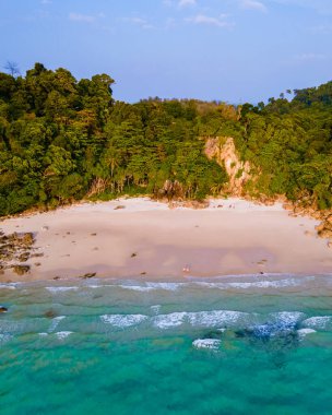 Tayland 'ın Koh Kradan adasındaki kumsalda güneş batımında palmiye ağaçlarıyla sahilde yürüyen bir çift kadın ve erkek İHA görüntüsü.