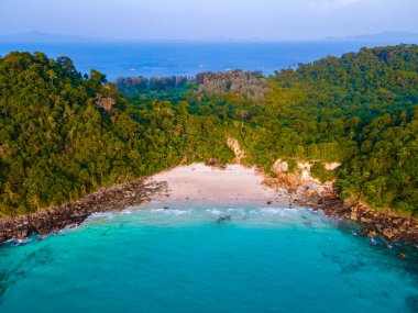 Tayland 'da Koh Kradan adasının kumsalında güneşli bir günde, gün batımı kumsalında yürüyen bir çift kadın ve erkek İHA görüntüsü.