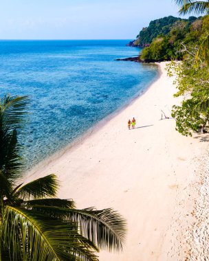 Tayland 'da Koh Kradan adasının kumsalında birkaç kadın ve erkeğin palmiye ağaçlarıyla kumsalda yürüdüğü drone görüntüsü.