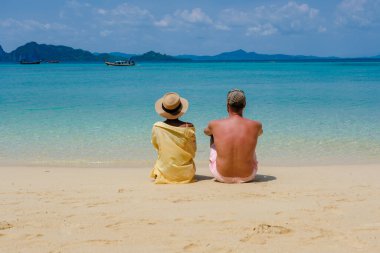 Tatil sırasında Tayland 'daki Koh Kradan adasında oturan bir çift kadın ve erkeğin arkası.