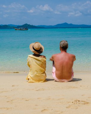 Tatil sırasında Tayland 'daki Koh Kradan adasında oturup okyanusu izleyen bir çift kadın ve erkeğin arkasında.