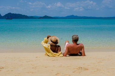 Tatil sırasında Tayland 'daki Koh Kradan adasında oturup okyanusu izleyen bir çift kadın ve erkeğin arkasında.