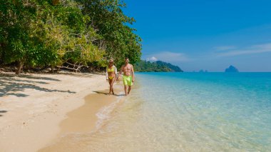 Tatilin güneşli bir gününde, Tayland 'daki Koh Kradan adasının sahilinde oturan birkaç erkek ve kadının arkası.