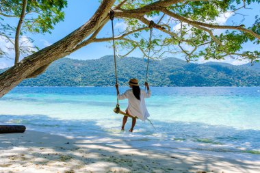 Koh Lipe Adası 'nın güney Tayland sahilindeki bir salıncakta sallanan bir kadın turkuaz renkli bir okyanus ve Ko Lipe' deki beyaz kumlu plajda. Tarutao Ulusal Parkı, Koh Rawi Adası