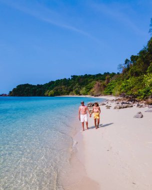 Beyaz tropikal bir plaj ve turkuaz renkli bir okyanusla Koh Kradan Adası sahilinde yürüyen bir çift. Tayland 'da güneşli bir günde kumsalda kadınlar ve erkekler