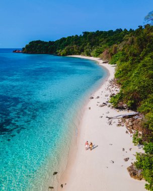 Beyaz tropikal bir plaj ve turkuaz renkli bir okyanusla Koh Kradan Adası sahilinde yürüyen bir çift. Tayland 'da güneşli bir günde kumsalda kadınlar ve erkekler