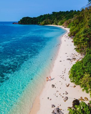 Beyaz tropikal bir plaj ve turkuaz renkli bir okyanusla Koh Kradan Adası sahilinde yürüyen bir çift. Erkekler ve kadınlar yukarıdan Tayland 'da tatil sırasında İHA ile görülmüşler.