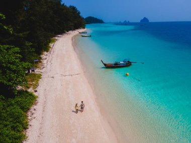 Beyaz tropikal bir plaj ve turkuaz renkli bir okyanusla Koh Kradan Adası sahilinde yürüyen bir çift. Tayland 'da güneşli bir günde kumsalda kadınlar ve erkekler