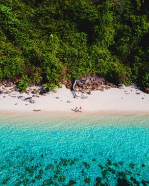 Beyaz tropikal bir plaj ve turkuaz renkli bir okyanusla Koh Kradan Adası sahilinde yürüyen bir çift. Kumsaldaki kadın ve erkekler yukarıdan drone ile görüldüler.