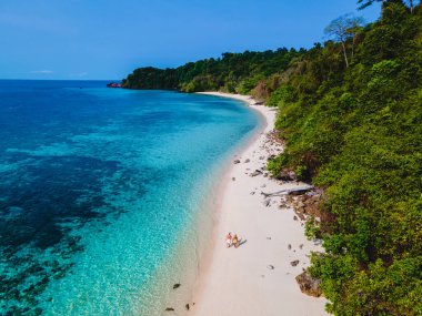 Beyaz tropikal bir plaj ve turkuaz renkli bir okyanusla Koh Kradan Adası sahilinde yürüyen bir çift. Kumsaldaki kadın ve erkekler yukarıdan drone ile görüldüler.