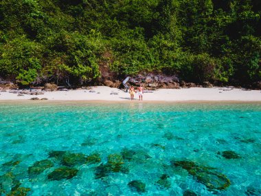 Beyaz tropikal bir plaj ve turkuaz renkli bir okyanusla Koh Kradan Adası sahilinde yürüyen bir çift. Tayland 'da güneşli bir günde kumsalda kadınlar ve erkekler