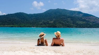 Koh Lipe Adası Tayland sahilinde bir çift, mavi okyanusu ve beyaz yumuşak kumu olan tropik bir ada. Ko Lipe Adası Tayland. Erkekler ve kadınlar sahilde dinlenip okyanusa bakıyorlar.
