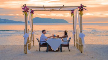 Romantic dinner on the beach in Phuket Thailand, couple man and woman mid age Asian woman and European man having dinner on the beach in Thailand during sunset at vacation clipart