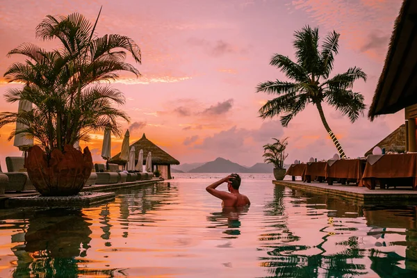 young men in a swimming pool during sunset, Luxury swimming pool in a tropical resort, relaxing holidays in Seychelles islands. La Digue, a Young guy during sunset by swim pool