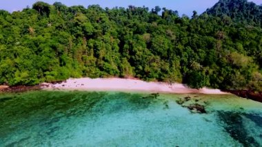 Güneşli bir günde kumsalın yukarısındaki bir drondan görülen turkuaz renkli bir okyanusla Koh Kradan Adası sahilinde bir çift kadın ve erkek.