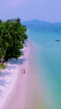 Koh Mook Adası ya da Koh Muk Trat Tayland palmiye ağaçları olan tropikal beyaz bir plaj. Tayland 'da tatilde olan bir çift adam ve kadın sahilde yürüyorlar.