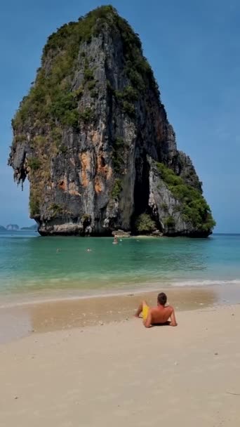 レイルバイビーチクラビタイ レイルバイクラビの熱帯ビーチ タイの牧歌的なレイルバイビーチのパノラマビュー晴れた日に短い泳ぎでビーチでリラックスした若い男性 — ストック動画