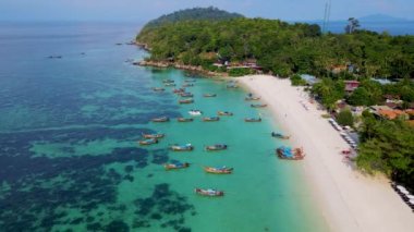 Tayland 'ın Koh Lipe şehrinde güneşli bir günde, turkuaz renkli okyanusta uzun kuyruklu teknelerin Koh Lipe Adası manzarası. Kumsaldaki hava aracı görüntüsü.
