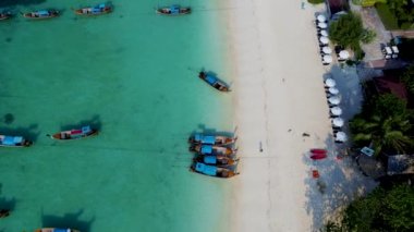 Tayland 'daki Koh Lipe Adası' nda güneşli bir günde turkuaz renkli okyanusta uzun kuyruklu teknelerin hava manzarası. Kumsaldaki hava aracı görüntüsü.