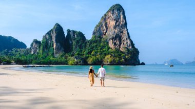 Tayland Railay Beach Krabi 'de tatilde plajda dinlenen ve arka planda güzel kireçtaşı kayalıkları olan bir çift kadın ve erkek.