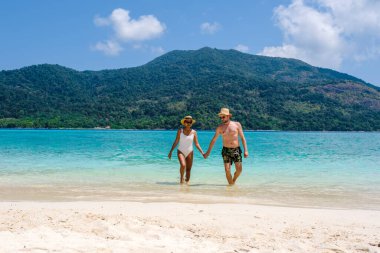 Birkaç erkek ve kadın tropikal Koh Lipe Güney Tayland sahilinde yürüyorlar. Renkli turkuaz renkli okyanusları olan tropikal beyaz bir sahil.
