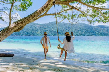 Güney Tayland 'da Ko Ra Wi Adası sahilinde salıncakta sallanan bir çift. Turkuaz renkli okyanus Tarutao Ulusal Parkı, Koh Rawi, Tambon Ko Tarutao
