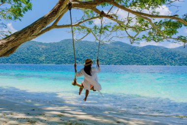 Ko Ra Wi Adası 'nın güney Tayland sahilinde salıncakta sallanan kadınlar, Tarutao Ulusal Parkı, Koh Rawi, Tambon Ko Tarutao' da turkuaz renkli okyanusları olan tropik beyaz kumlu plajlar.