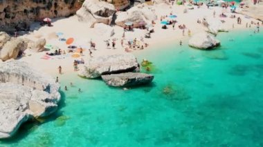 Cala Mariolu Plajı Sardinya İtalya, plaj şemsiyeleriyle dolu güzel bir plaj ve güneşlenen ve turkuaz suda yüzen insanlar. Cala Gonone Baunei, Sardinya, İtalya Golfo Di Orosei