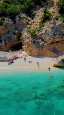 Cala Mariolu plajı, Cala Biriola ve Cala Goloritze yakınları, Baunei, Sardinya, İtalya yaz boyunca insanlar çakıl taşı plajında güneşlenirken