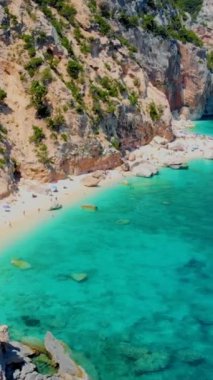 Cala Mariolu plajı, Cala Biriola ve Cala Goloritze yakınları, Baunei, Sardinya, İtalya yaz boyunca insanlar çakıl taşı plajında güneşlenirken