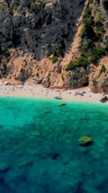 Cala Mariolu plajı, Cala Biriola ve Cala Goloritze yakınları, Baunei, Sardinya, İtalya yaz boyunca insanlar çakıl taşı plajında güneşlenirken