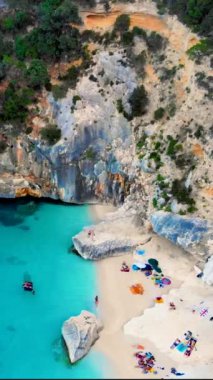 Yaz boyunca Cala Goloritze plajı, Baunei, Sardinya, İtalya Golfo Di Orosei Cala Gonone, plajın yukarısından güneşlenen insanlarla insansız hava aracı manzarası