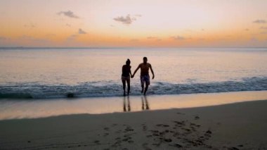 Saint Lucia Castries plajı yukarıdan lüks otellerle dolu, gün batımında mavi turkuaz renkli okyanuslu St. Lucia tropikal adası. Gün batımında sahilde yürüyen bir çift kadın ve erkek.