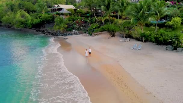 サンルシアのビーチ豪華なホテル 日没時に青いタークス色の海を持つセントルシアの熱帯の島 夕暮れ時に男と女のカップルがビーチを歩く — ストック動画