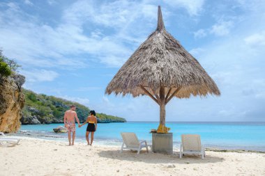 Curacao, Cas Abao Beach Playa Cas Abao Karayip adası Curacao, Playa Cas Abao tropikal beyaz plajlı plajda plaj sandalyeleri ve mavi turkuvaz renkli okyanusu olan bir çift kadın ve erkek.. 