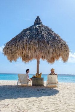 Curacao, Cas Abao Beach Playa Cas Abao Karayip adası Curacao, Playa Cas Abao tropik beyaz plaj sandalyeli ve plaj şemsiyeli bir çift kadın ve erkek. 