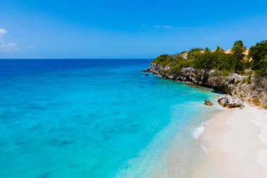 Playa Kalki Plajı Karayip adası Curacao, Playa Kalki Curacao, mavi turkuaz renkli okyanuslu beyaz plaj. Kumsalın üstünde kumsal sandalyeleri ve şemsiyeleri olan insansız hava aracı manzarası.