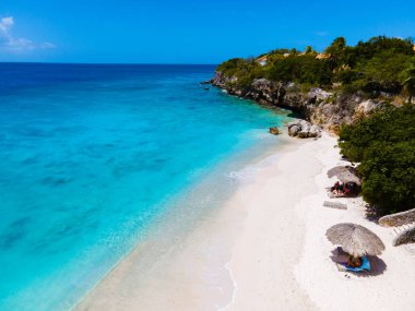 Playa Kalki Plajı Karayip adası Curacao, Playa Kalki Curacao, mavi turkuaz renkli okyanuslu beyaz plaj. Kumsalın üstünde kumsal sandalyeleri ve şemsiyeleri olan insansız hava aracı manzarası.