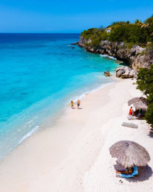 Curacao 'daki Playa Kalki, mavi turkuaz renkli okyanuslu beyaz plaj. Kumsaldaki bir çift kadın ve erkeğin hava görüntüsü.