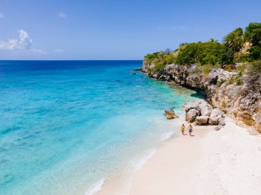 Curacao 'daki Playa Kalki, mavi turkuaz renkli okyanuslu beyaz plaj. Kumsaldaki bir çift kadın ve erkeğin hava görüntüsü.