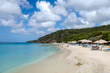 Grote Knip Beach Curacao Adası Mart 2021, Karayip adası Curacao Karayipleri 'nde tropikal plajlar, plaj sandalyelerinde şemsiye altında güneşlenen turistler.