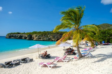 Grote Knip Beach Curacao Adası Mart 2021, Karayip adası Curacao Karayipleri 'nde tropikal plajlar, plaj sandalyelerinde şemsiye altında güneşlenen turistler.