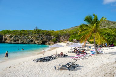 Grote Knip Beach Curacao Adası Mart 2021, Karayip adası Curacao Karayipleri 'nde tropikal plajlar, plaj sandalyelerinde şemsiye altında güneşlenen turistler.